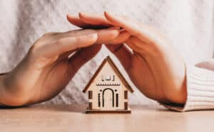 woman-holds-protects-wooden-house-with-her-hands